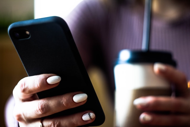 Image of a person holding a cup of coffee and a phone.